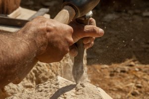 Guédelon: Ein Steinmetz behaut einen Mauerstein.